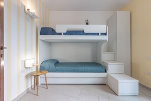 A bunk bed room with a desk and chair, a small stool, and a cabinet.