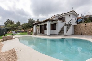 Una casa con piscina, patio cubierto y pared de piedra.