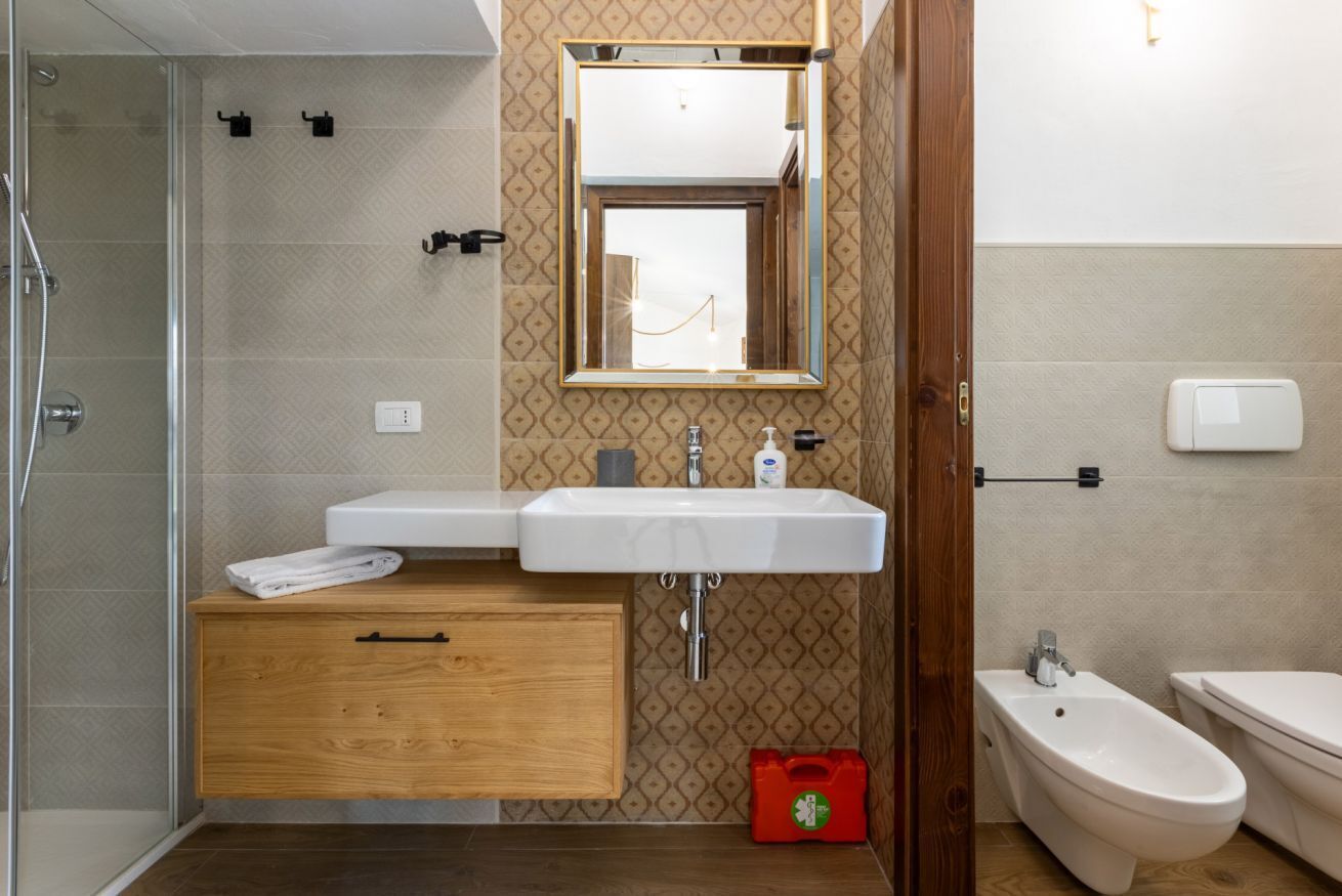 A bathroom with a shower, a sink with a mirror, a toilet, and a bidet.