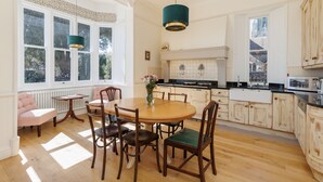 Een ruime keuken met houten kasten, een centraal eiland en een eethoek met stoelen en een tafel.