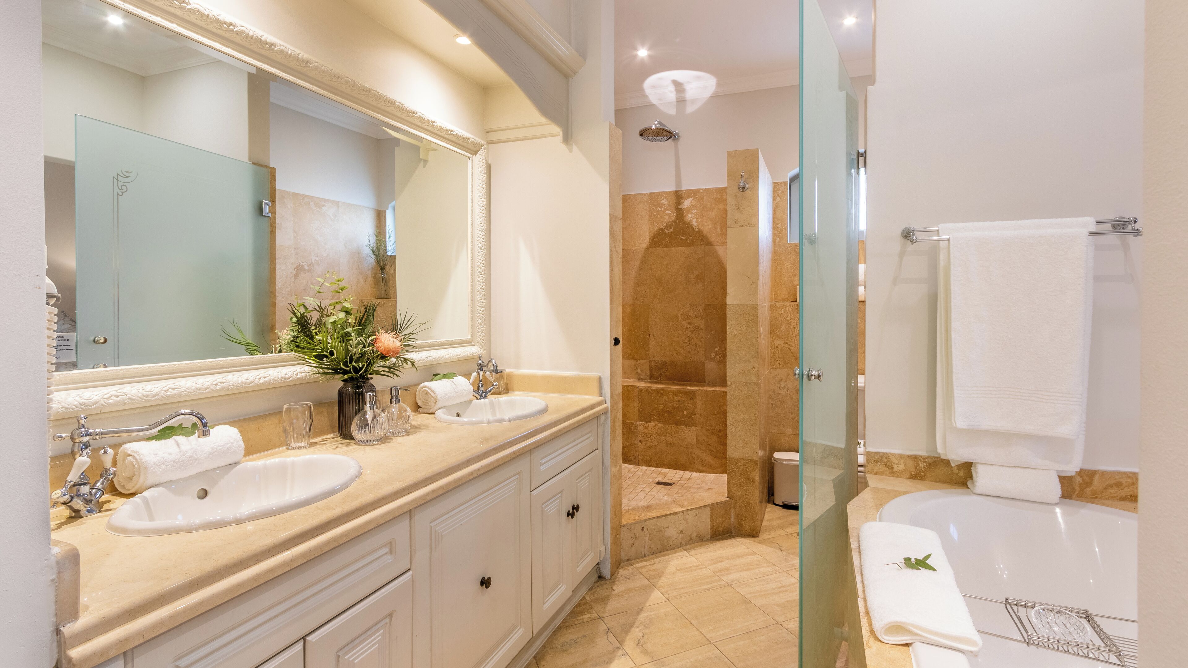 A modern bathroom with two sinks, a large mirror, a glass shower enclosure, and a bathtub.