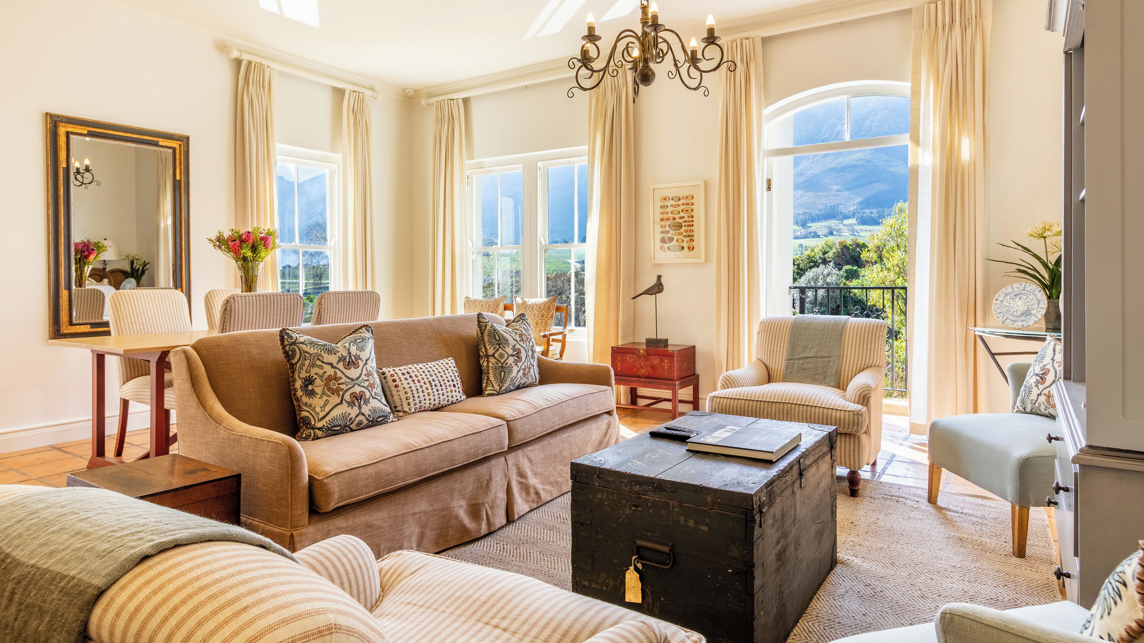 A spacious living room with a large sofa, armchairs, a wooden coffee table, and a view of the outdoors through large windows.