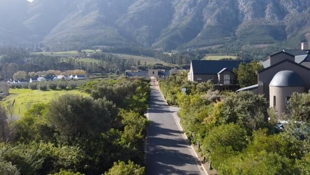 Una strada che attraversa una zona rurale, con case e montagne sullo sfondo.