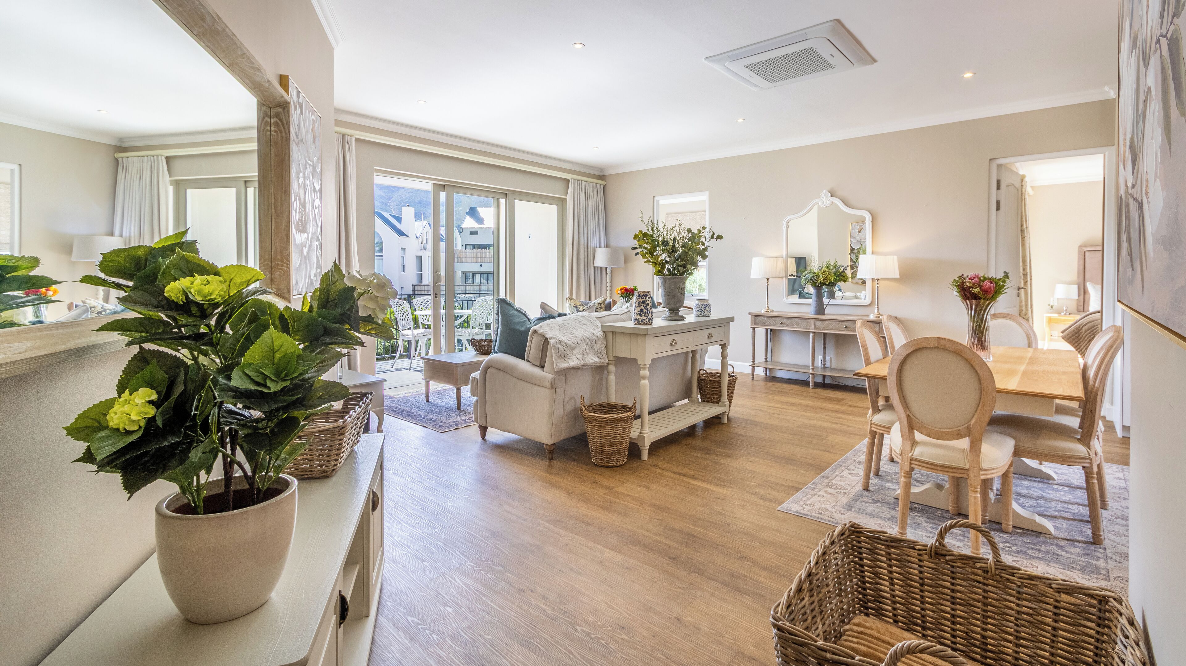 Amplia sala de estar con un ventanal grande, comedor con mesa y sillas de madera, y una zona de estar acogedora con sofá y planta en maceta.