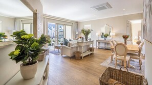 Ein geräumiges Wohnzimmer mit großem Fenster, einem Essbereich mit Holztisch und Stühlen sowie einer gemütlichen Sitzecke mit Sofa und Topfpflanze.