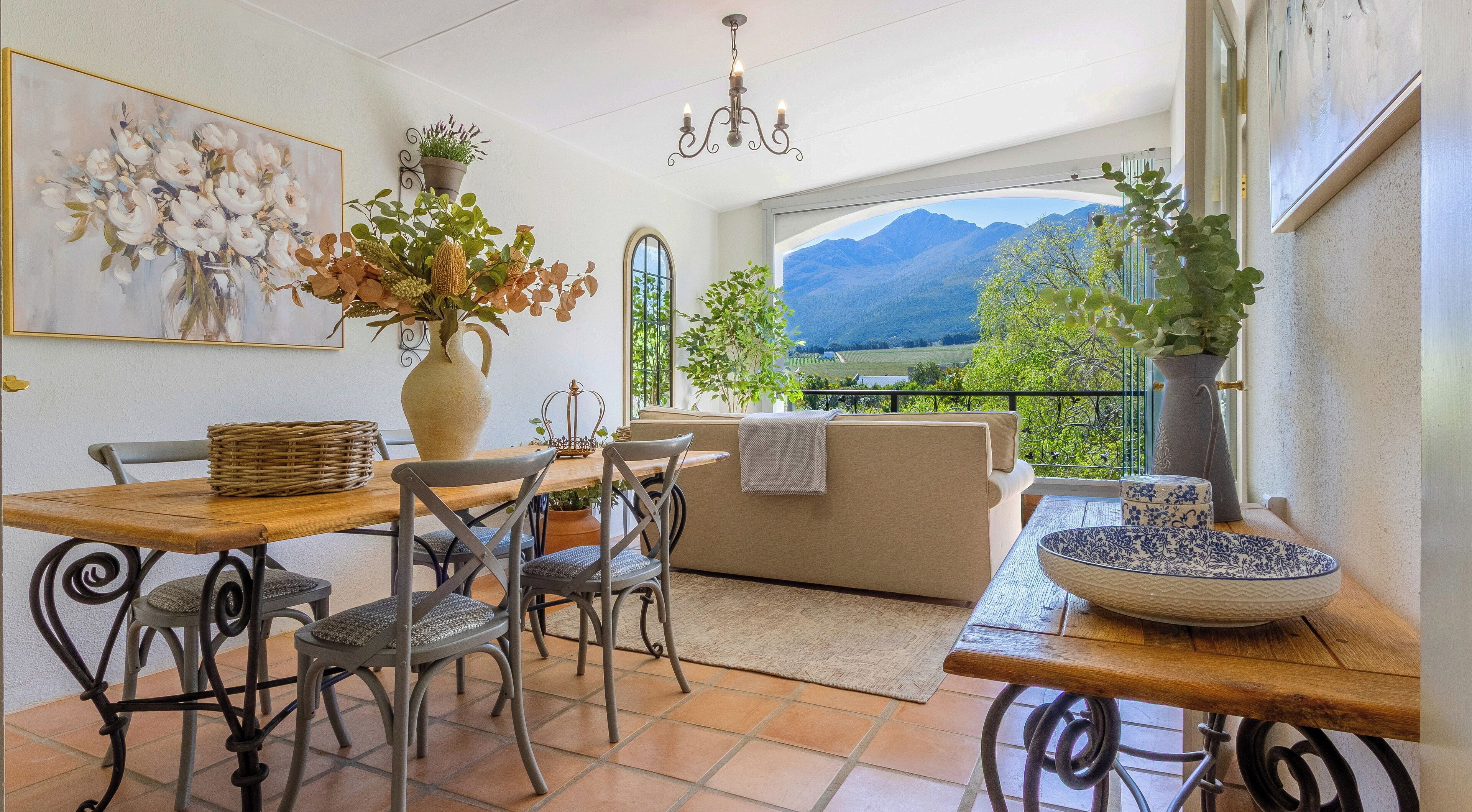 Un comedor con una mesa, sillas, un jarrón de flores, una araña y vistas a la montaña a través de una ventana.