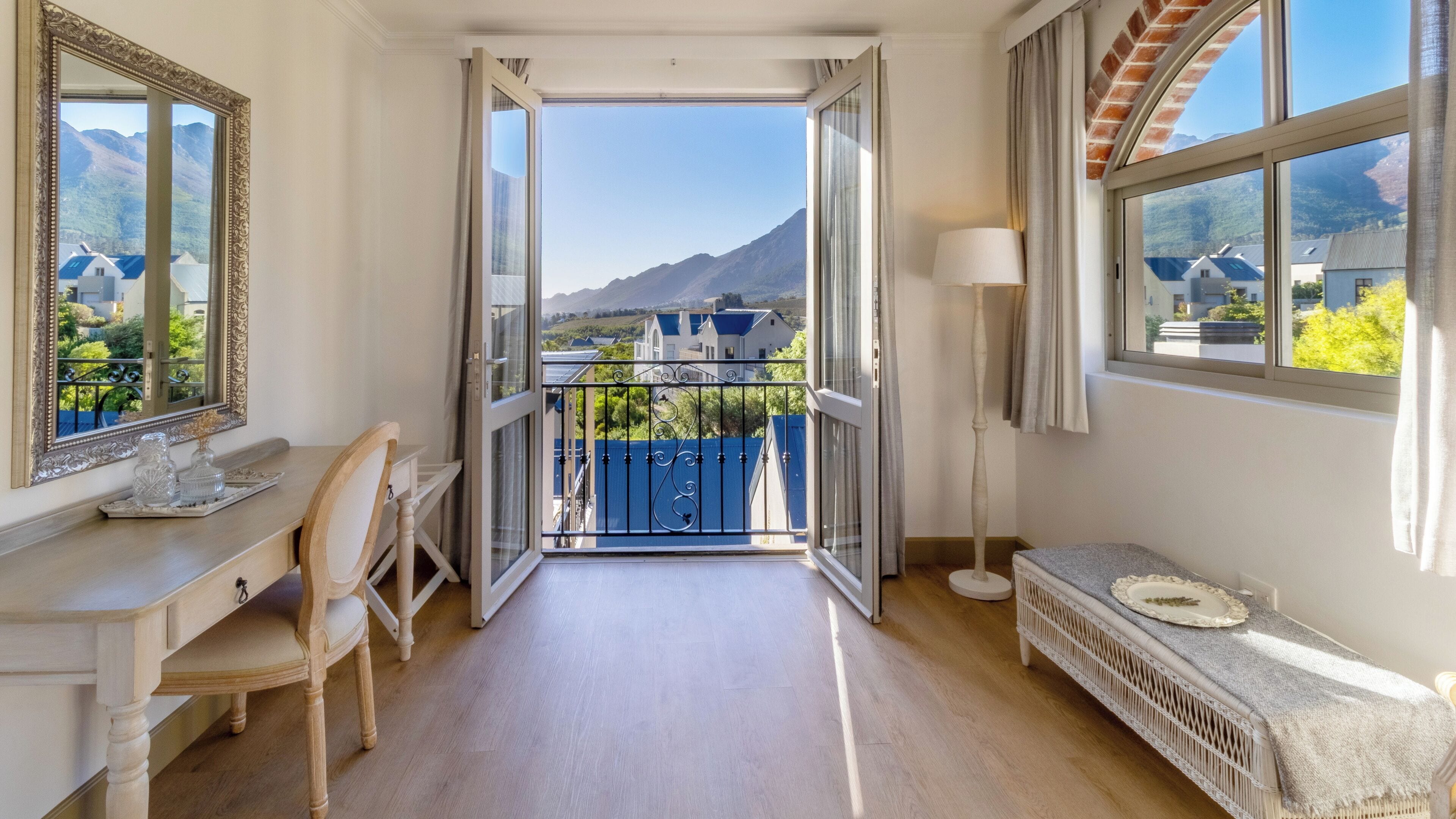 A room with a desk, chair, bedside table, and a view of mountains through an open door.