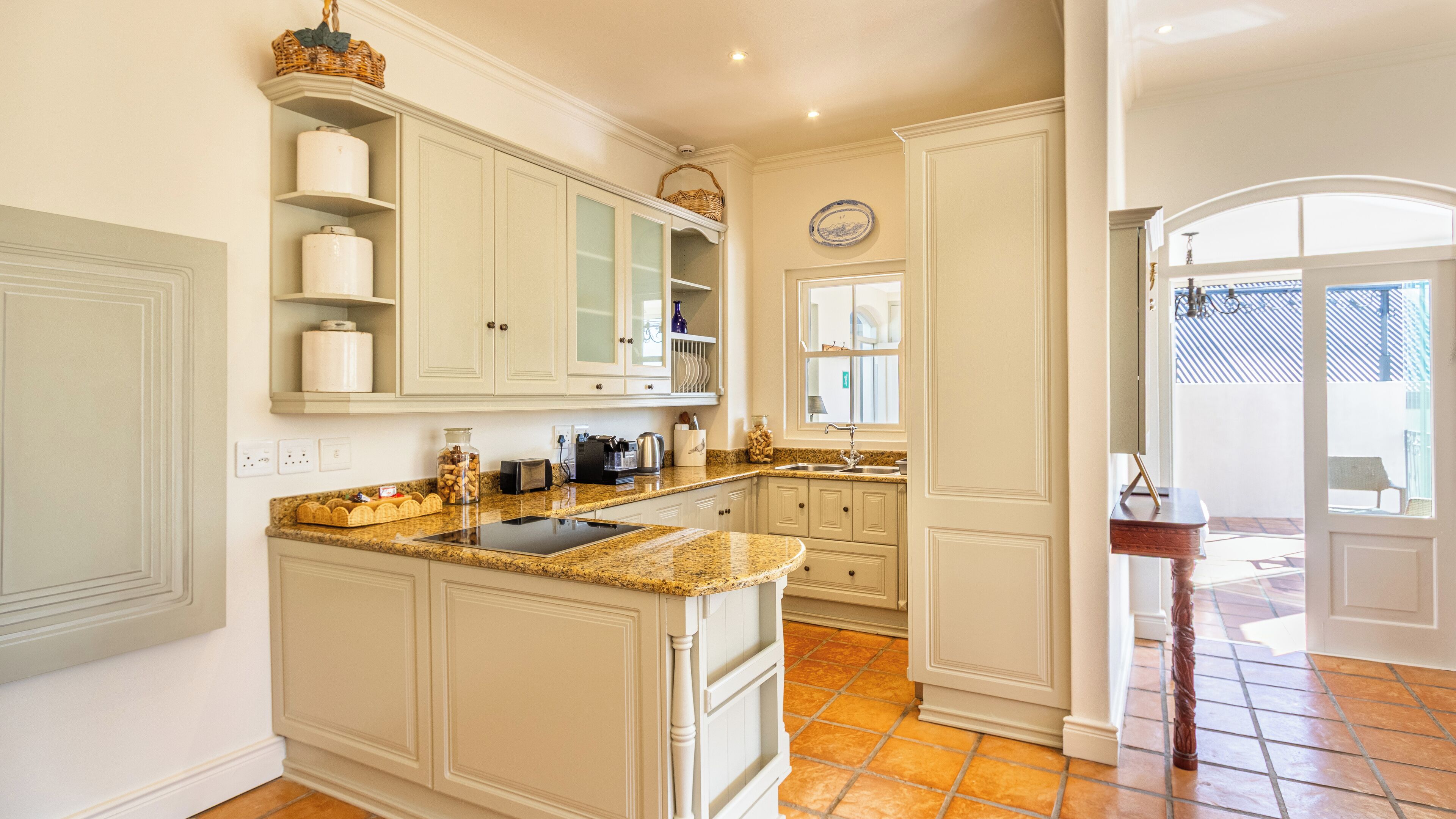 A spacious kitchen with white cabinetry, a granite countertop, and a central island. There are built-in shelves and a window providing natural light.