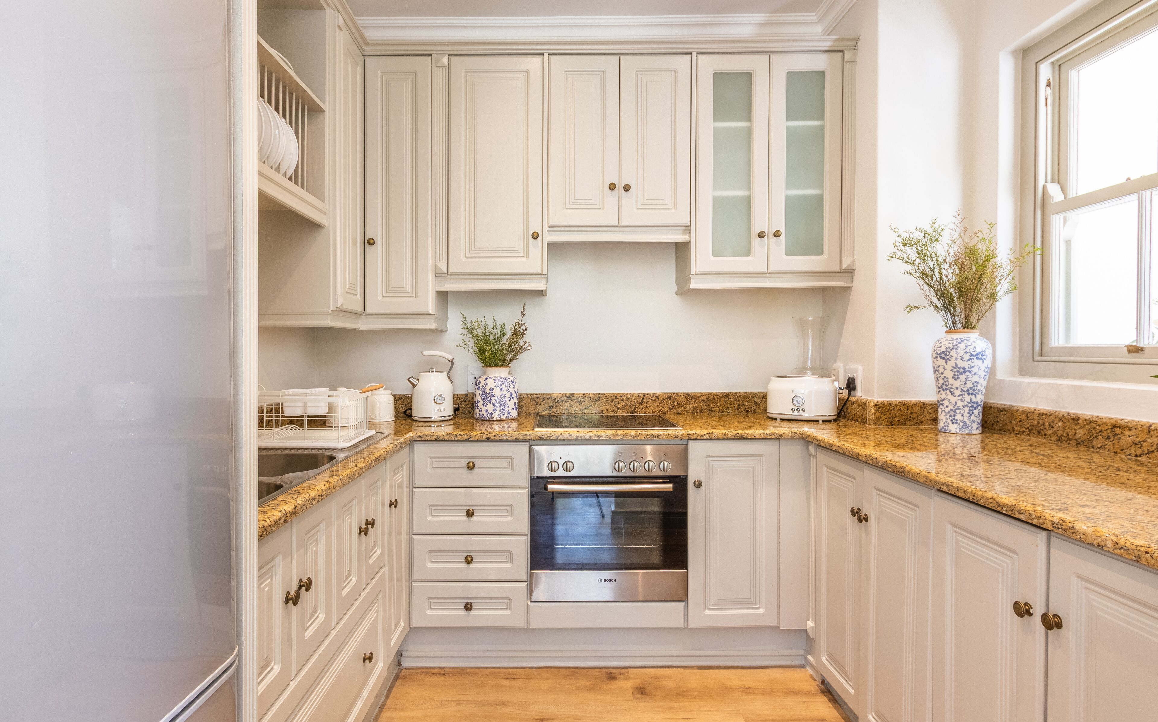 A kitchen with white cabinets, a Bosch oven, a granite countertop, and a window with a plant.