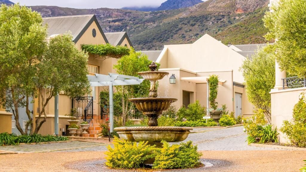A courtyard with a central fountain, surrounded by buildings with a mountain backdrop.