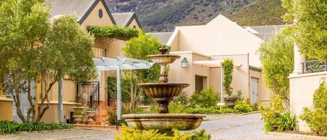 A courtyard with a central fountain, surrounded by buildings with a mountain backdrop.