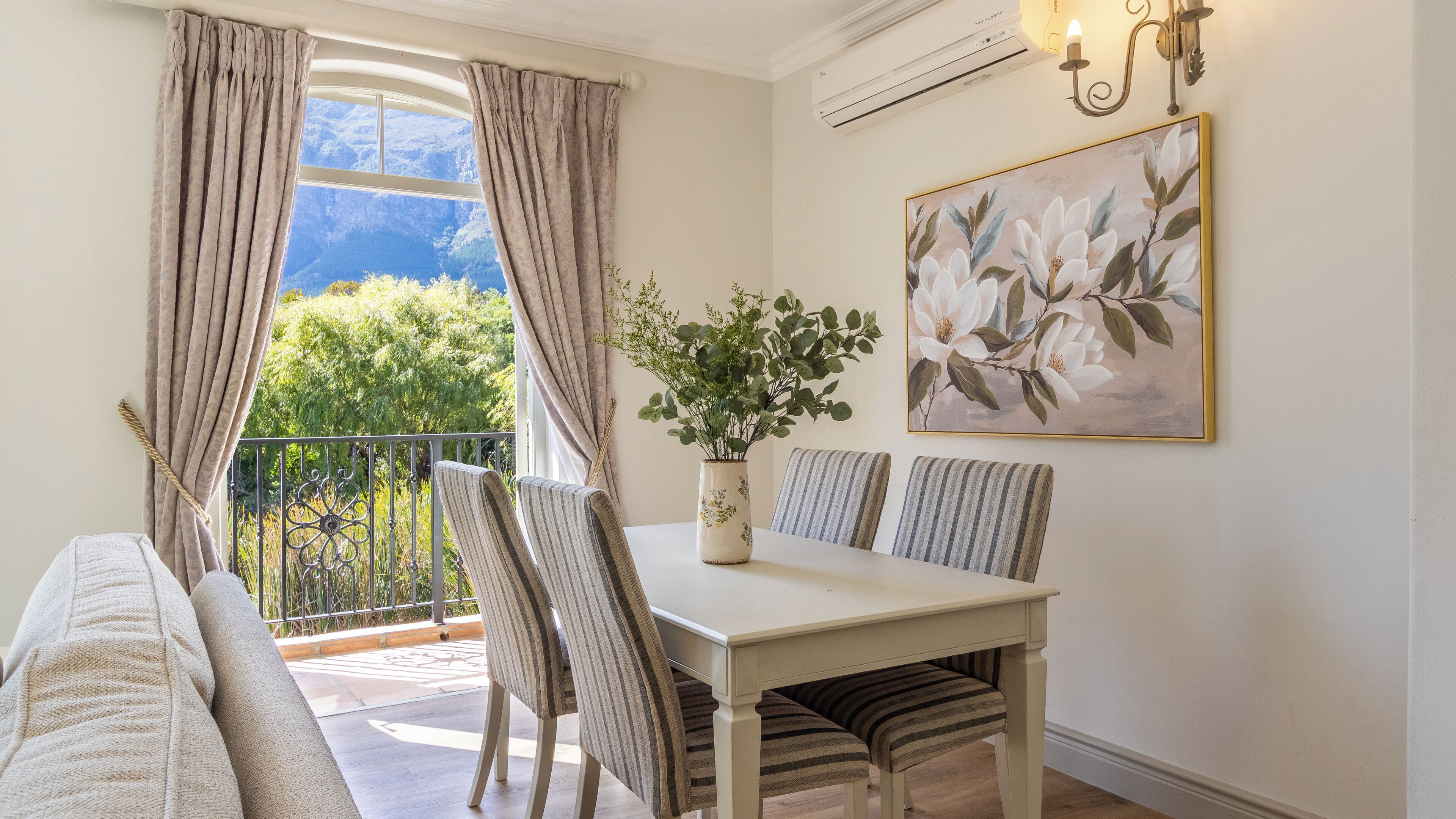 A dining area with a table, chairs, a vase with flowers, and a painting on the wall.