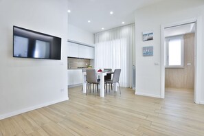 A modern kitchen with white cabinets, a dining area with a table and chairs, and a flat-screen TV mounted on the wall.