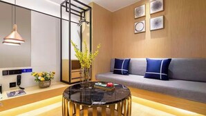 A modern living room with a sofa, a round coffee table, a vase with flowers, and a wall-mounted TV. - Z Holiday Hotel (Chengdu)