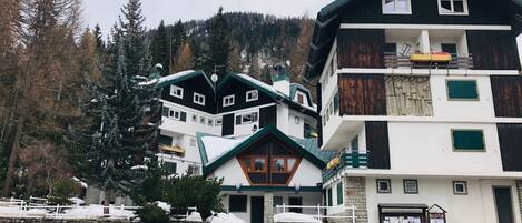 A multi-story building with a stone facade, a balcony, and a view of a forested mountain.