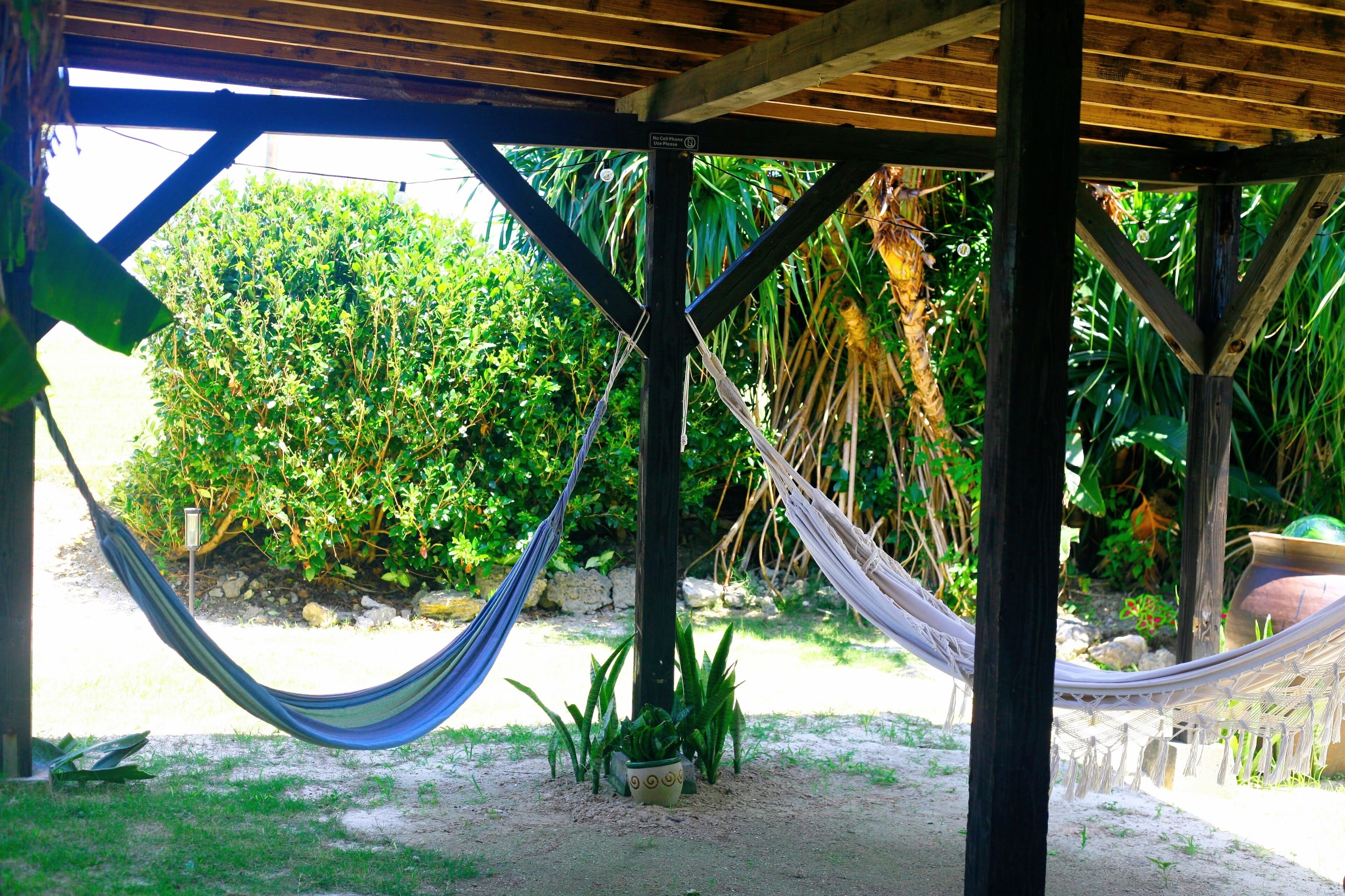 A hammock under a wooden structure with a view of a lush garden.