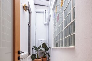 Un couloir étroit avec une porte blanche, une fenêtre grillagée et un chauffe-eau fixé au mur.