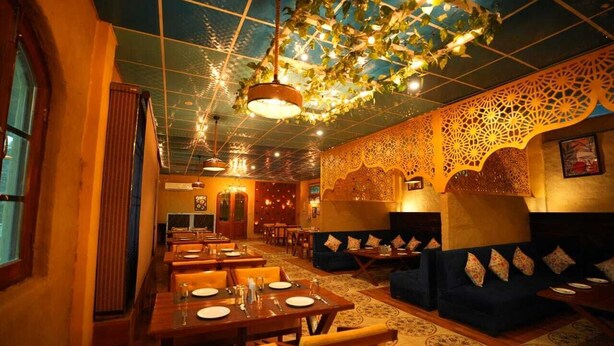 Un restaurante con mesas de madera y asientos acolchados azules, techo con diseño y paneles decorativos en las paredes.