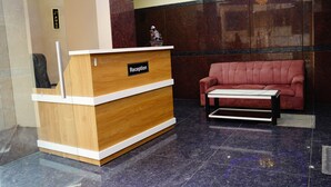 A reception desk with a 'Reception' sign, a red sofa, and a small table. - Royal Suites (Bangalore)