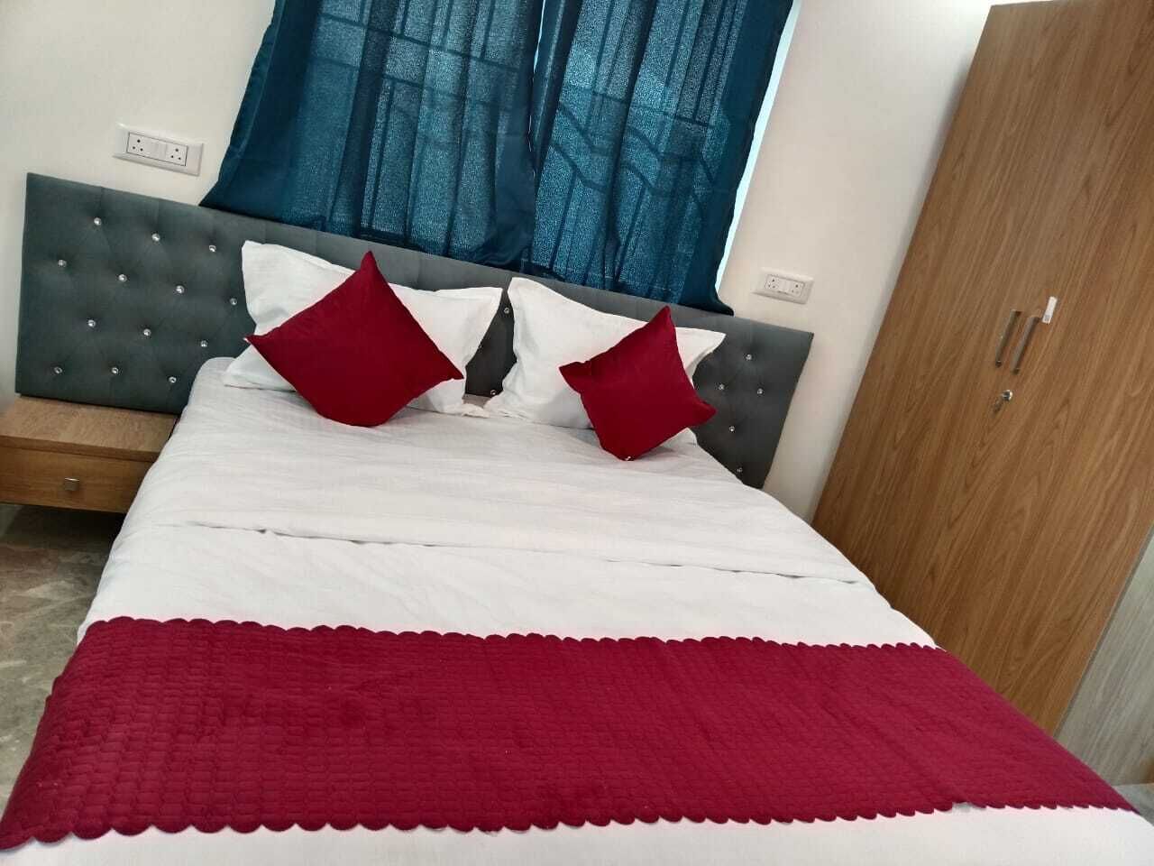 Una cama bien hecha con una colcha blanca y roja, dos almohadas rojas y un cabecero tapizado en gris.