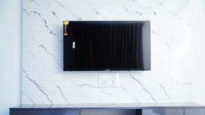A flat-screen TV mounted on a white marble wall with a black entertainment unit below. - Royal Suites (Bangalore)