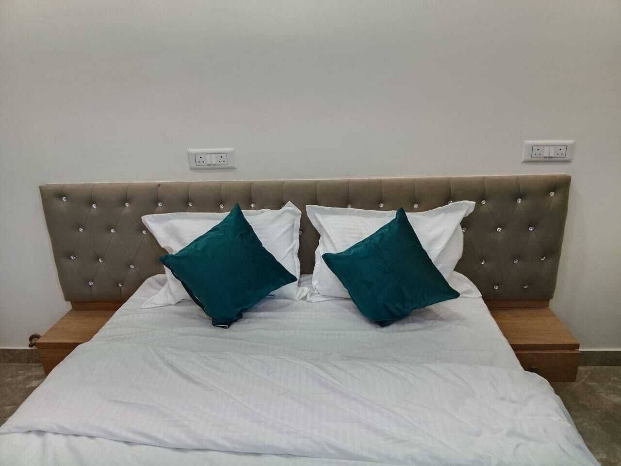 A bed with a tufted headboard, two white pillows, and two teal pillows.