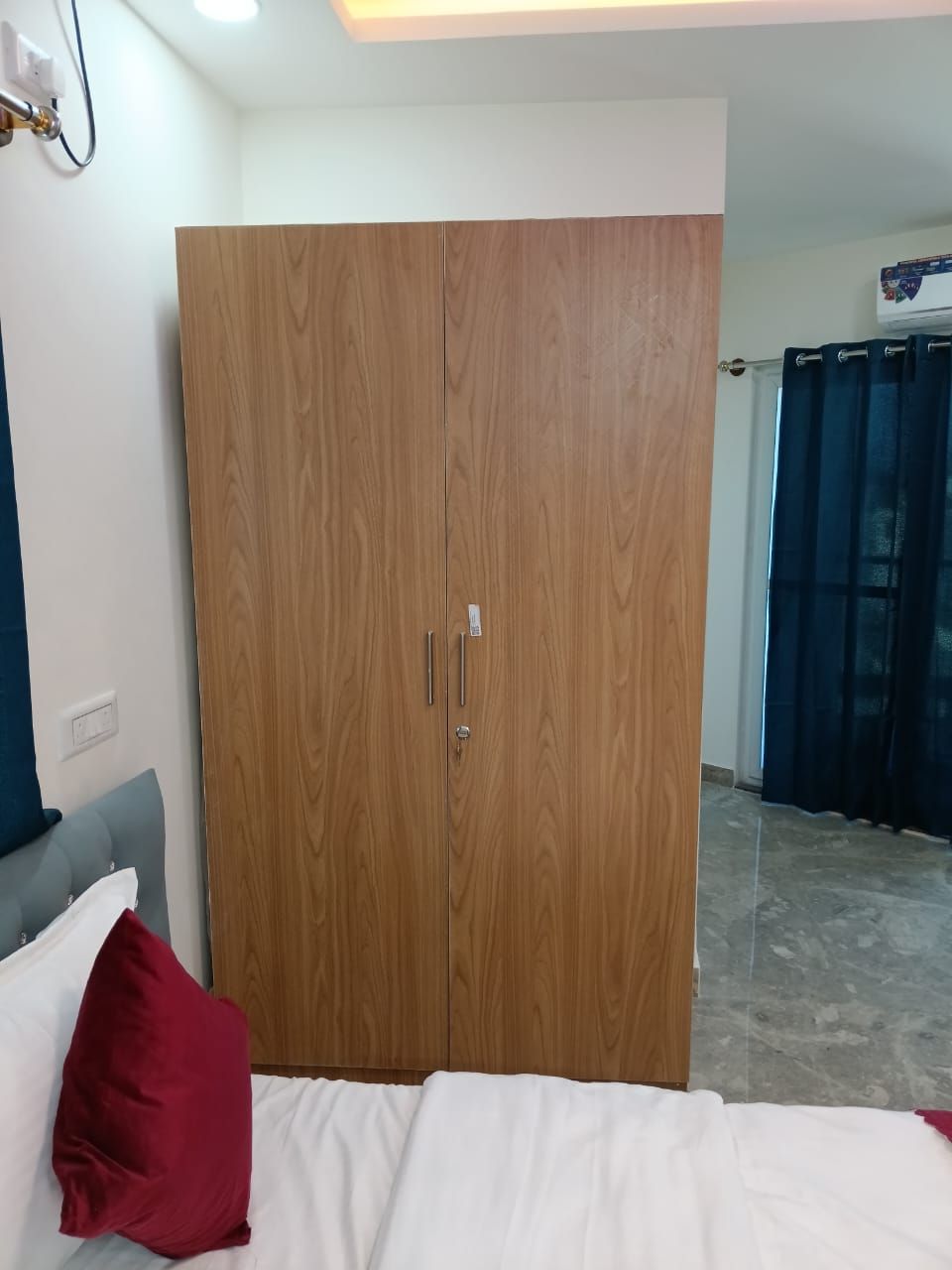 A bedroom with a wooden wardrobe, a bed with white and red bedding, and a grey headboard.