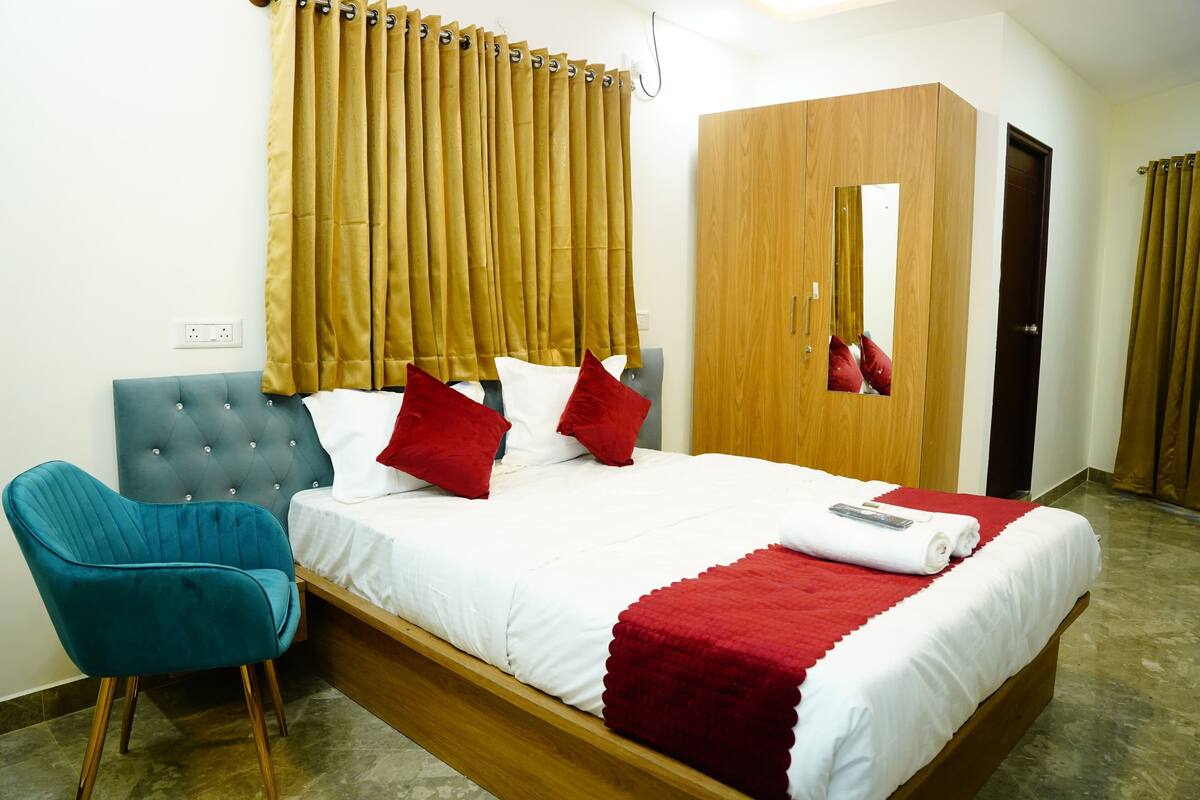 A bedroom with a bed, a blue chair, a wardrobe, and a mirror.
