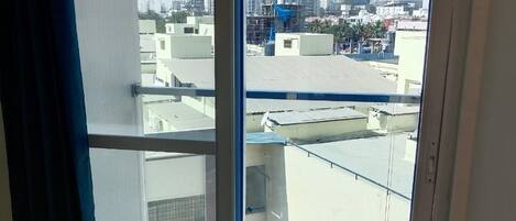 A room with a large sliding glass door leading to a balcony. The balcony has a metal railing and overlooks a cityscape with buildings and a clear sky.