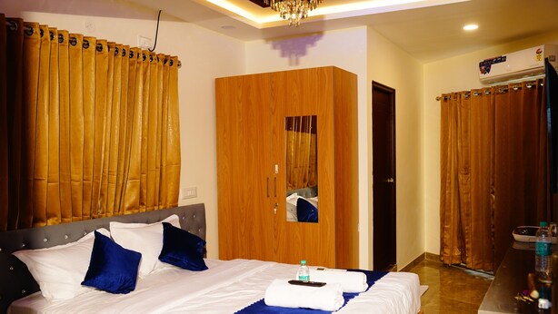A hotel room with a large bed, wooden wardrobe, and a bathroom with a shower curtain. - Royal Suites (Bangalore)