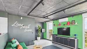 Un salon moderne avec un canapé vert, un néon, un téléviseur et un balcon offrant une vue dégagée.