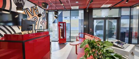 A modern reception desk with a red color scheme, a seating area with a red bench, and a large window offering a view of the outside.