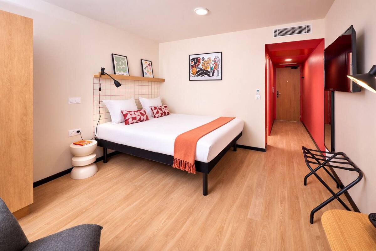 A modern hotel room with a bed, a desk, a chair, and a TV.