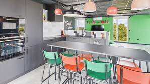 Une cuisine moderne dotée d’un grand îlot central, d’appareils électroménagers en acier inoxydable et de chaises aux couleurs vives.