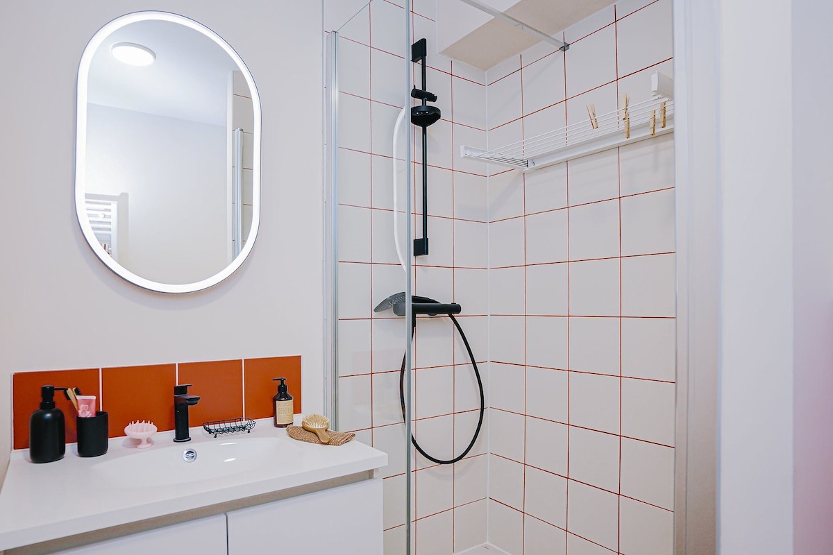 Ein modernes Badezimmer mit einem weißen Waschbecken, einem Spiegel und einer Dusche mit Duschbrause.