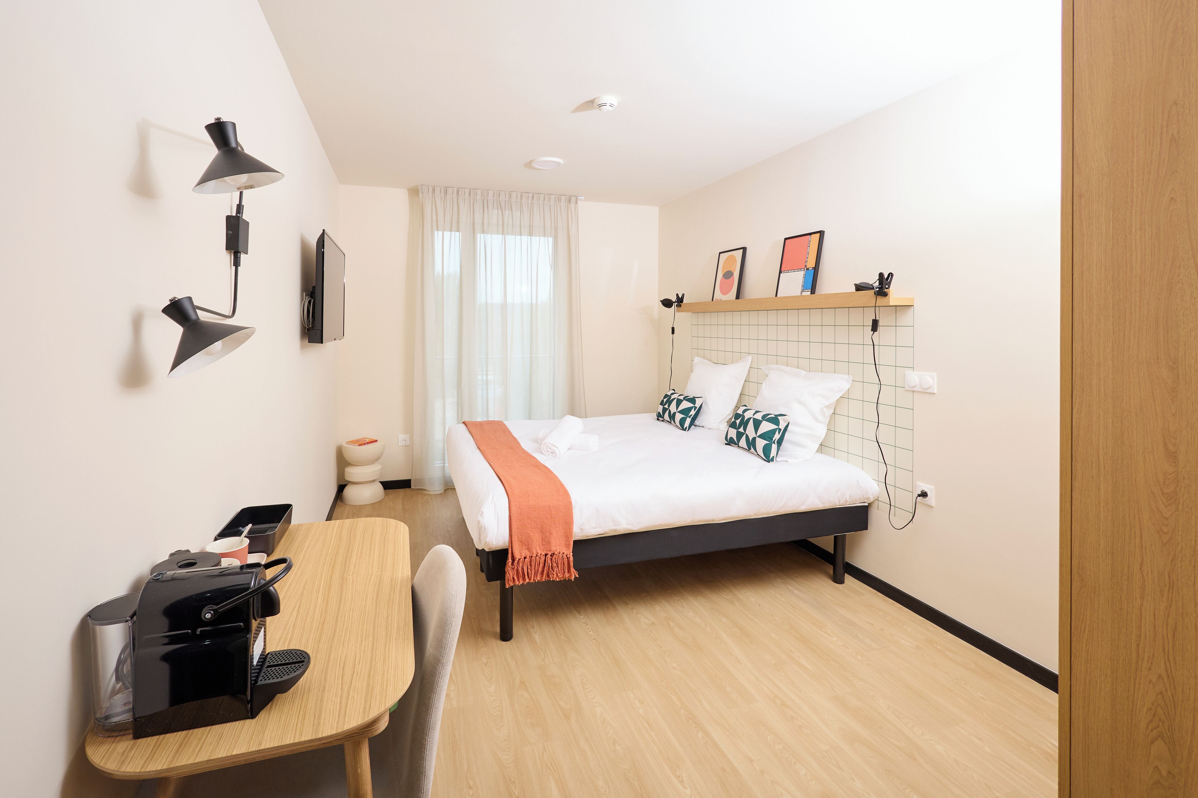 A modern hotel room with a bed, bedside table, desk, and a wall-mounted TV.
