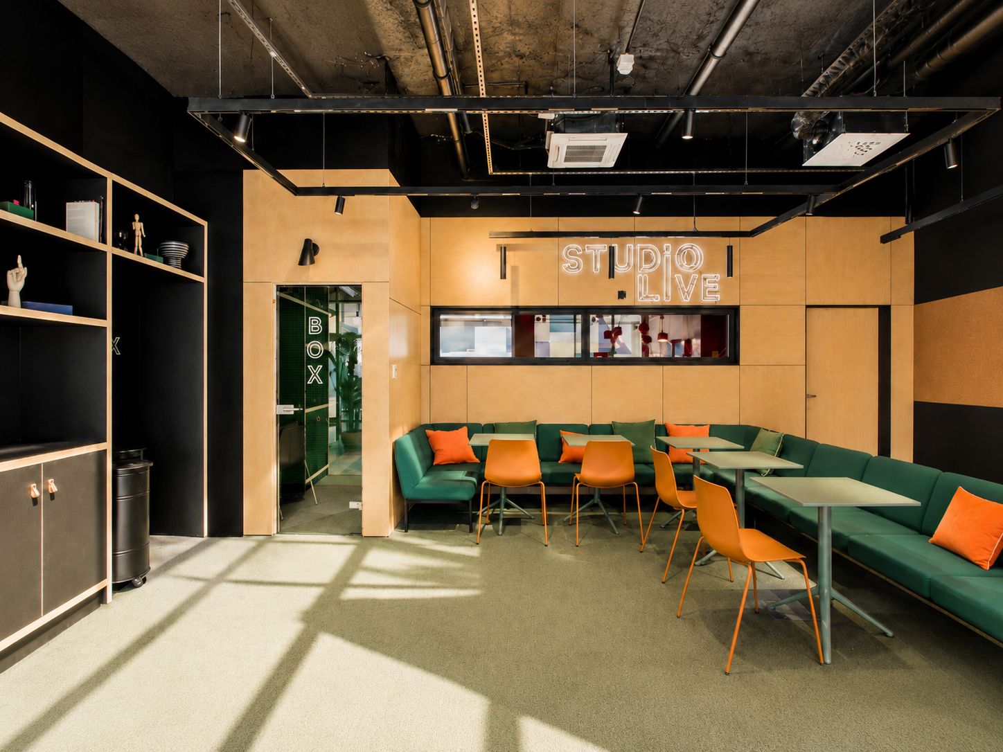 Een modern interieur met een lange groene bank, oranje fauteuils en een 'STUDIO LIVE' bord.