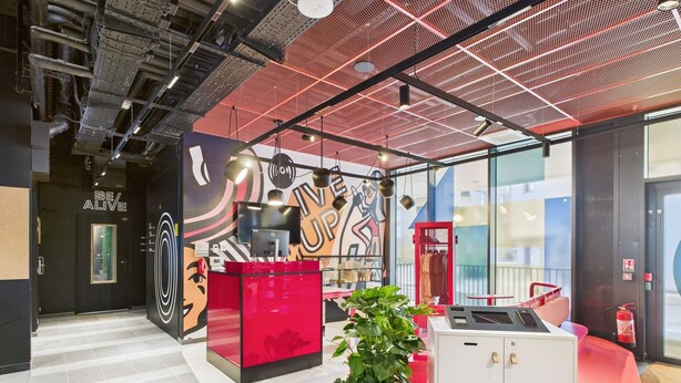 Un intérieur moderne aux couleurs rouge et blanche, agrémenté d’une grande plante et d’un espace bureau avec un ordinateur.