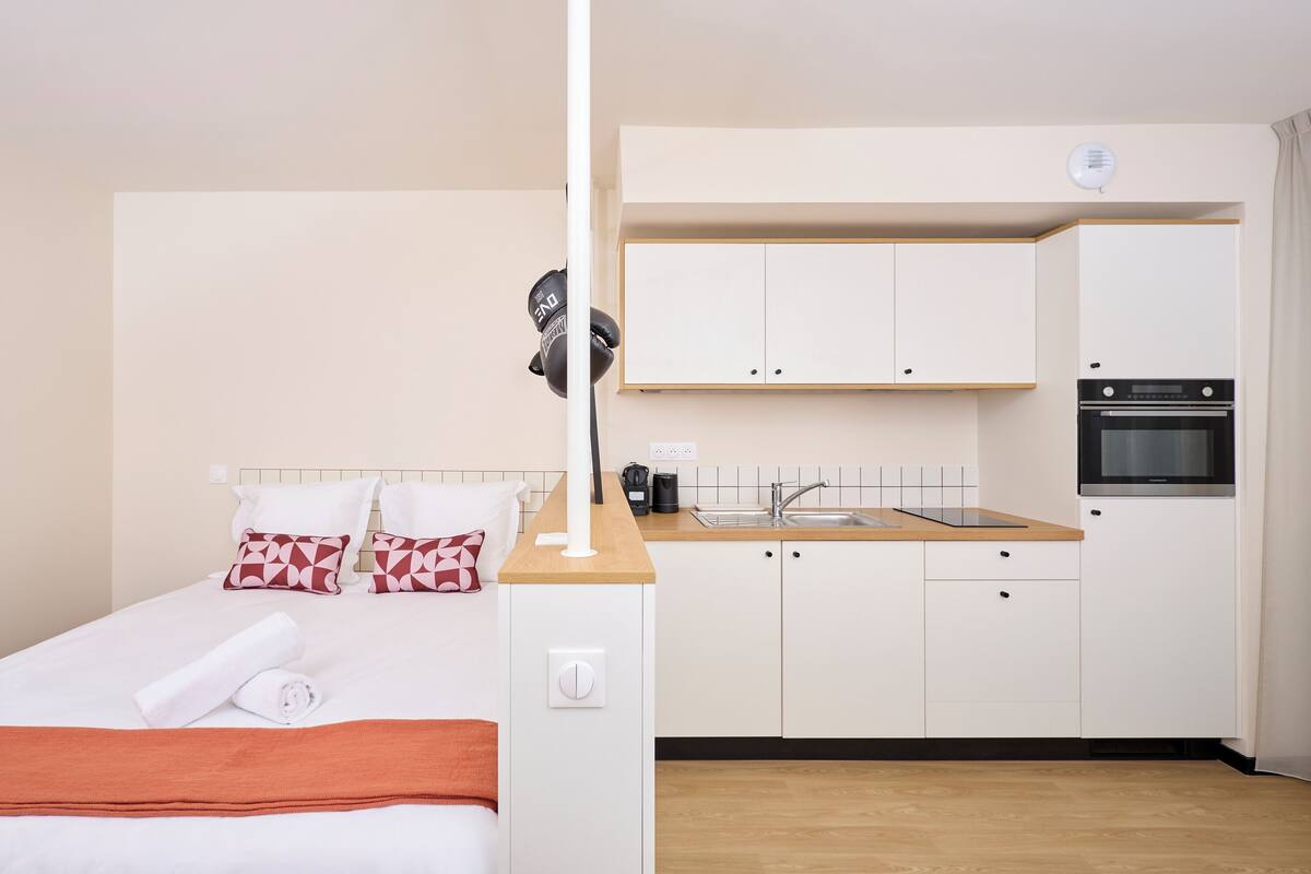 A compact hotel room with a bed, a small kitchenette, and a bathroom.