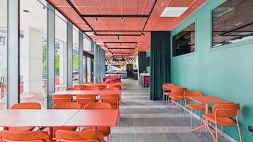 Un comedor interior moderno con mesas y sillas rojas, ventanas amplias y una pared de acento verde.