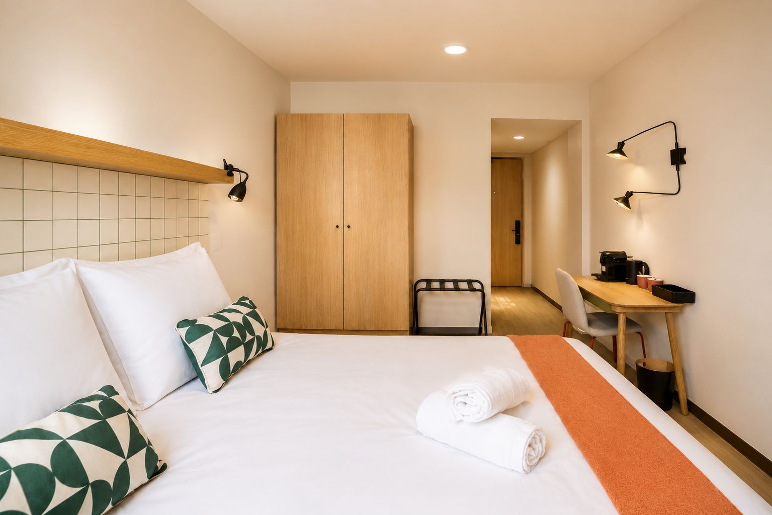 A hotel room with a bed, a desk, a chair, and a wardrobe.
