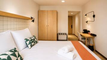 A hotel room with a bed, a desk, a chair, and a wardrobe.