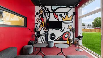 Una habitación con pared roja, un ventanal grande y un mural. Hay sofás grises y una pequeña mesa redonda.