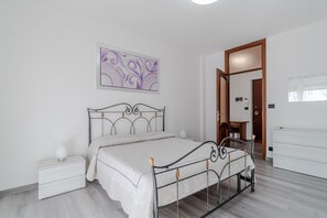 Un dormitorio con cama, mesita de noche, cómoda y una puerta que da a otra habitación.