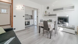 Ein modernes Wohnzimmer mit Sofa, Esstisch, Stühlen, Fernseher und einer Küche im Hintergrund.
