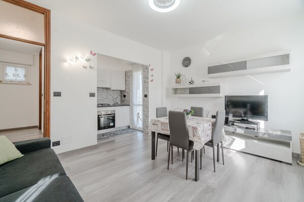 Una sala de estar moderna con un sofá, una mesa de comedor, sillas, un televisor y una cocina al fondo.