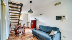 Una escalera con escalones de madera y barandillas de metal, una mesa de comedor con sillas, un sofá azul, un armario rojo y una lámpara colgante.