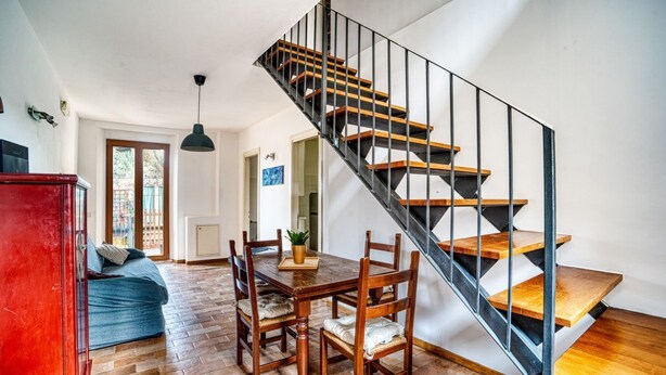 Un área de comedor con una mesa y sillas de madera, un armario rojo y una escalera con escalones de madera y barandillas de metal.