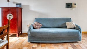 Una habitación con un sofá azul, una silla de madera, un armario rojo y un teléfono instalado en la pared.