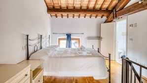Un dormitorio con techo de madera, cama con ropa de cama blanca, cómoda y ventana con cortinas azules.